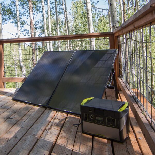 שני פאנלים סולאריים מתקפלים מדגם BOULDER 200B (12-22V, 200W) המוצגים על דק עץ ומחוברים לתחנת כוח ניידת, כשברקע עצים ומעקה מתכת - פתרון אידיאלי לייצור חשמל פוטו-וולטאי יעיל ותשתית אחסון אנרגיה מתחדשת בת קיימא.